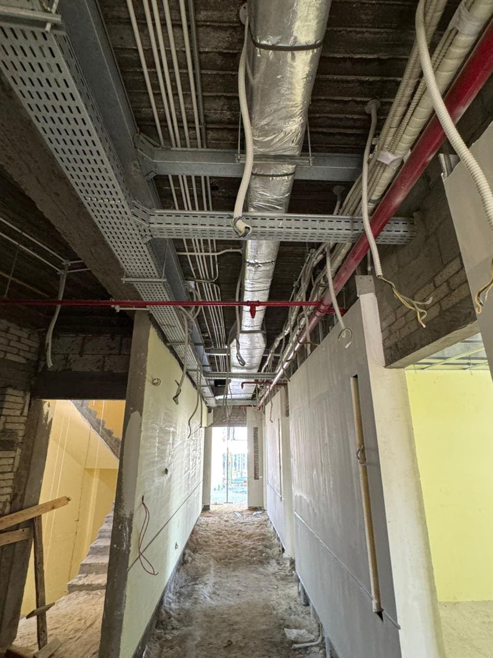 Perforated cable trays, flexible conduit, insulated ductwork and a red firefighting main running the length of a corridor above head height