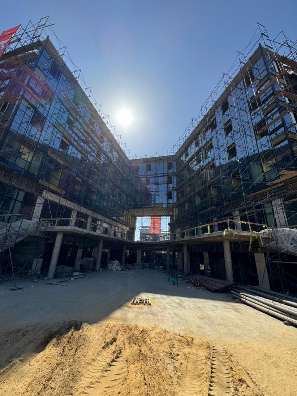 The scaffolded courtyard elevation of the development, dark glazed curtain walling installed around a sand-covered yard