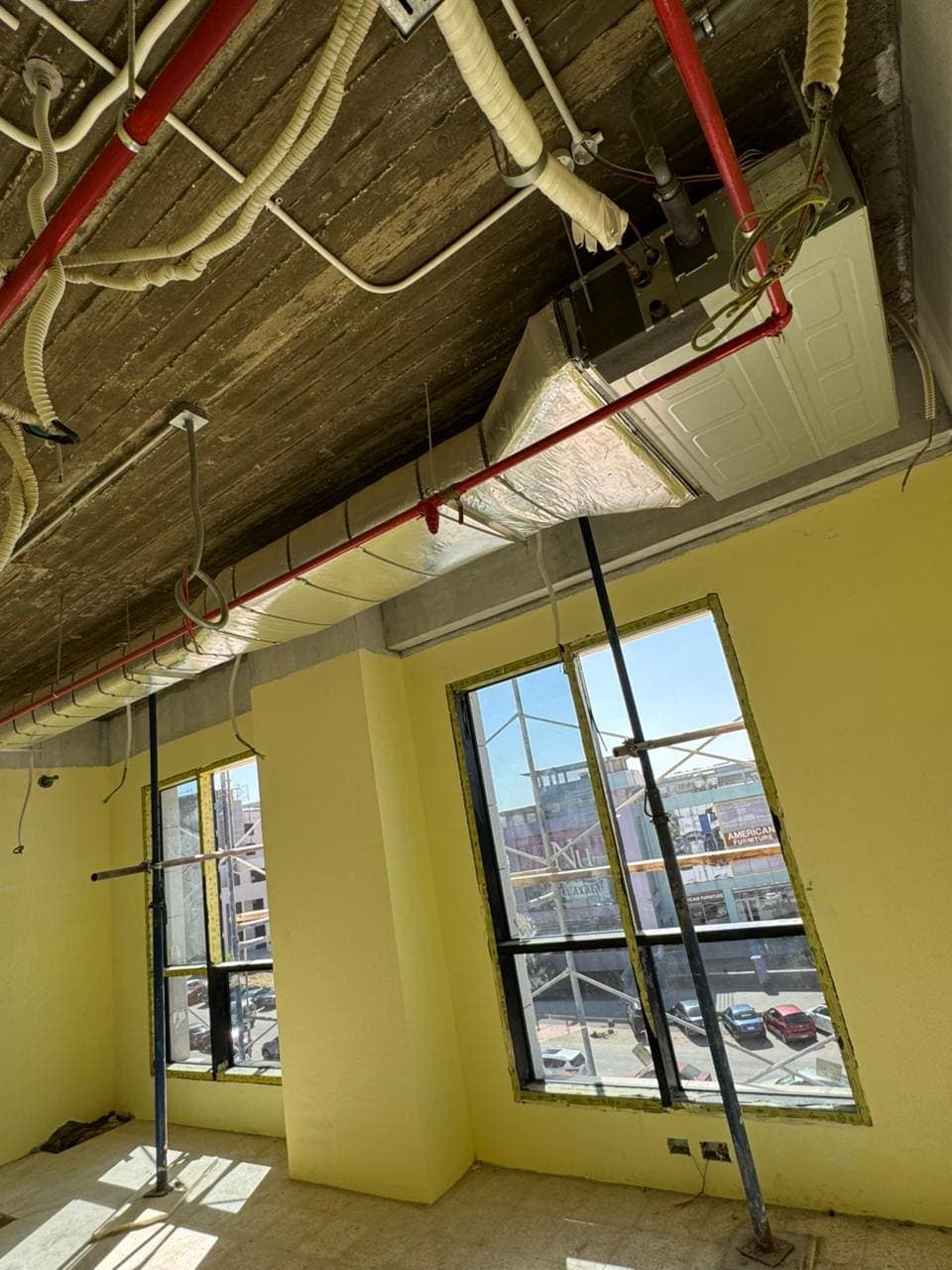 A ducted fan-coil unit, insulated ductwork and red firefighting pipework above the window openings of a corner unit