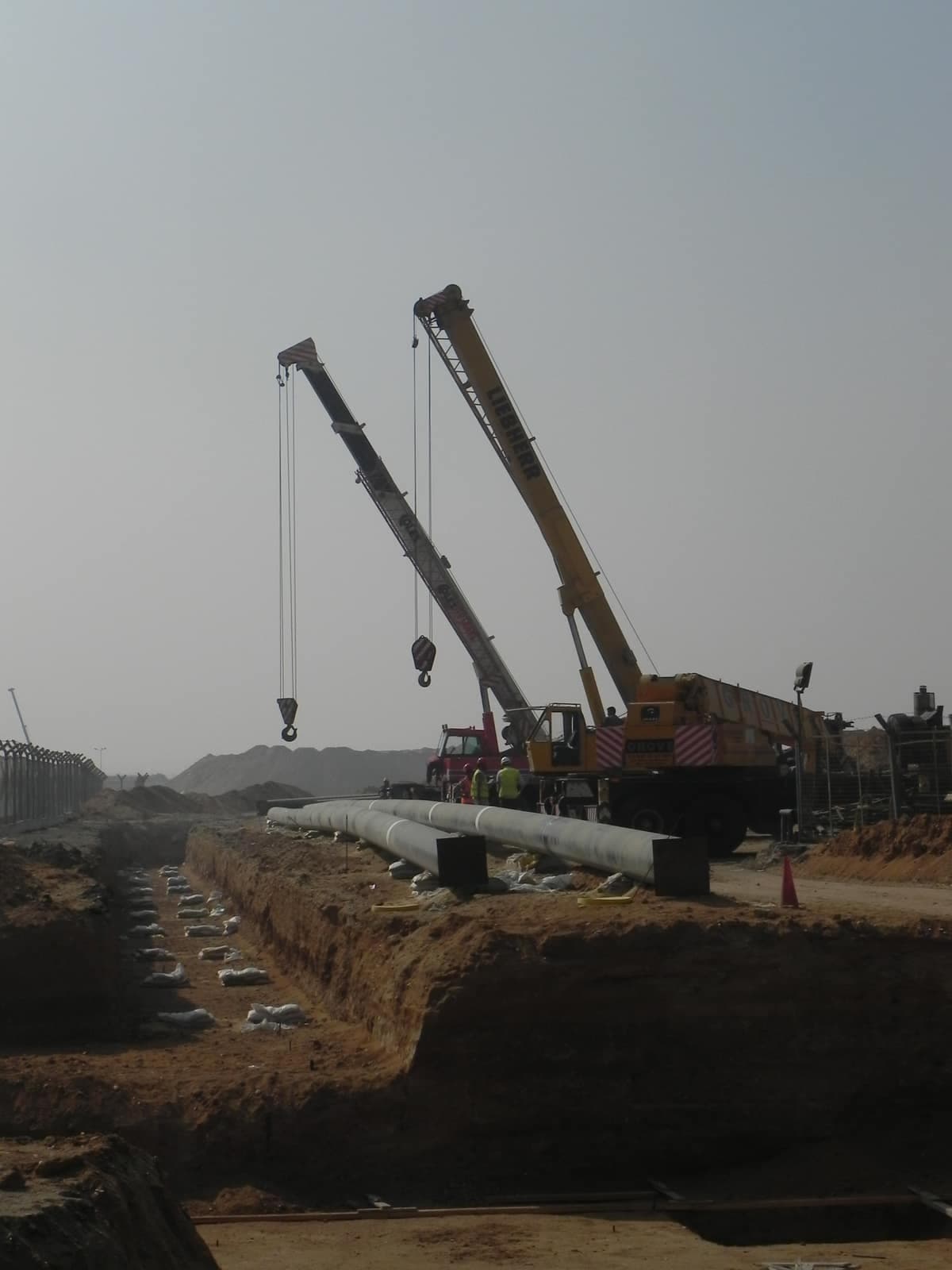 A mobile crane lowering a coated hydrant main into an open trench at Cairo Airport Terminal 2