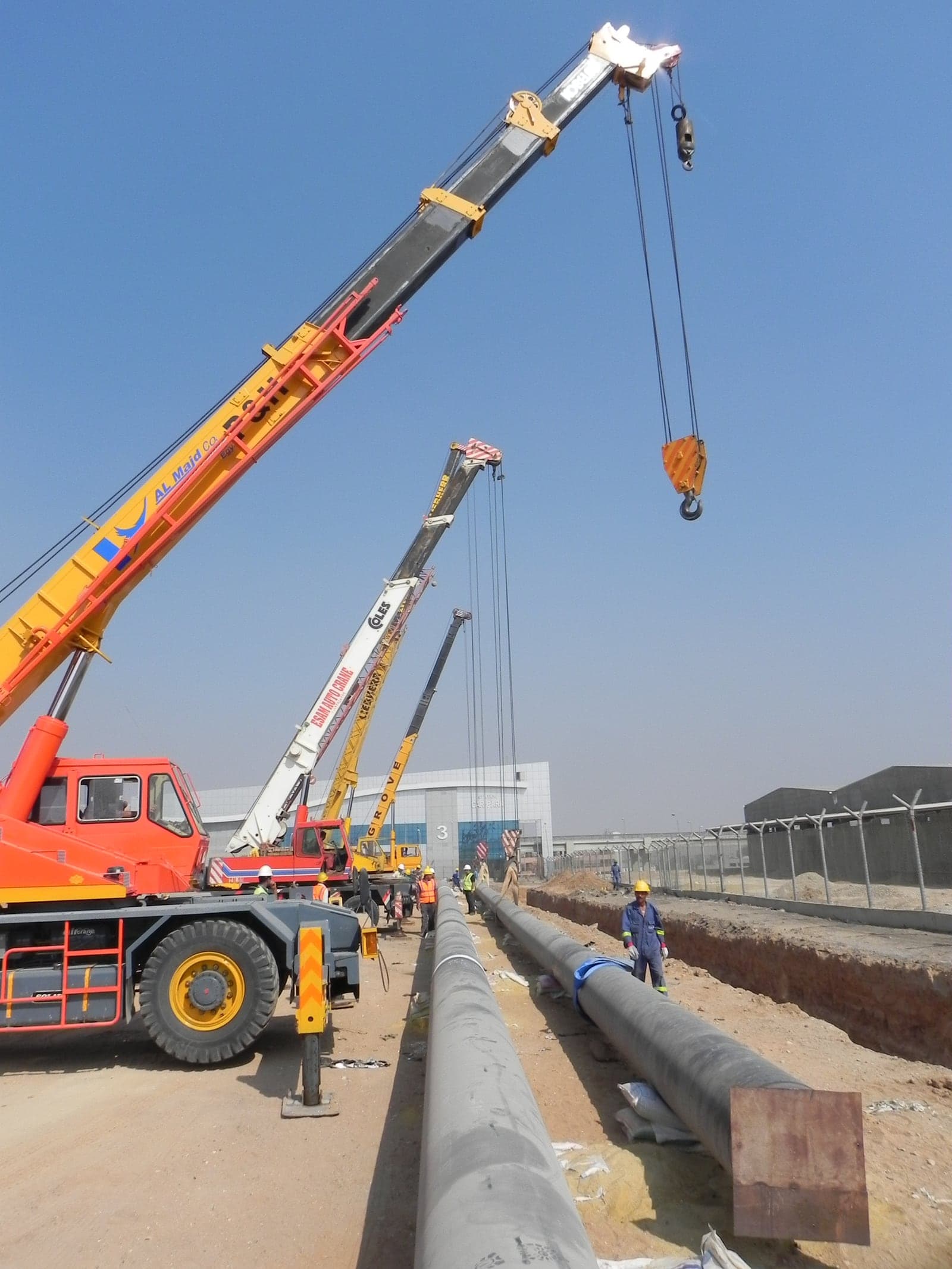 Cranes lowering large-diameter hydrant mains into the trench beside the terminal buildings at Cairo Airport Terminal 2