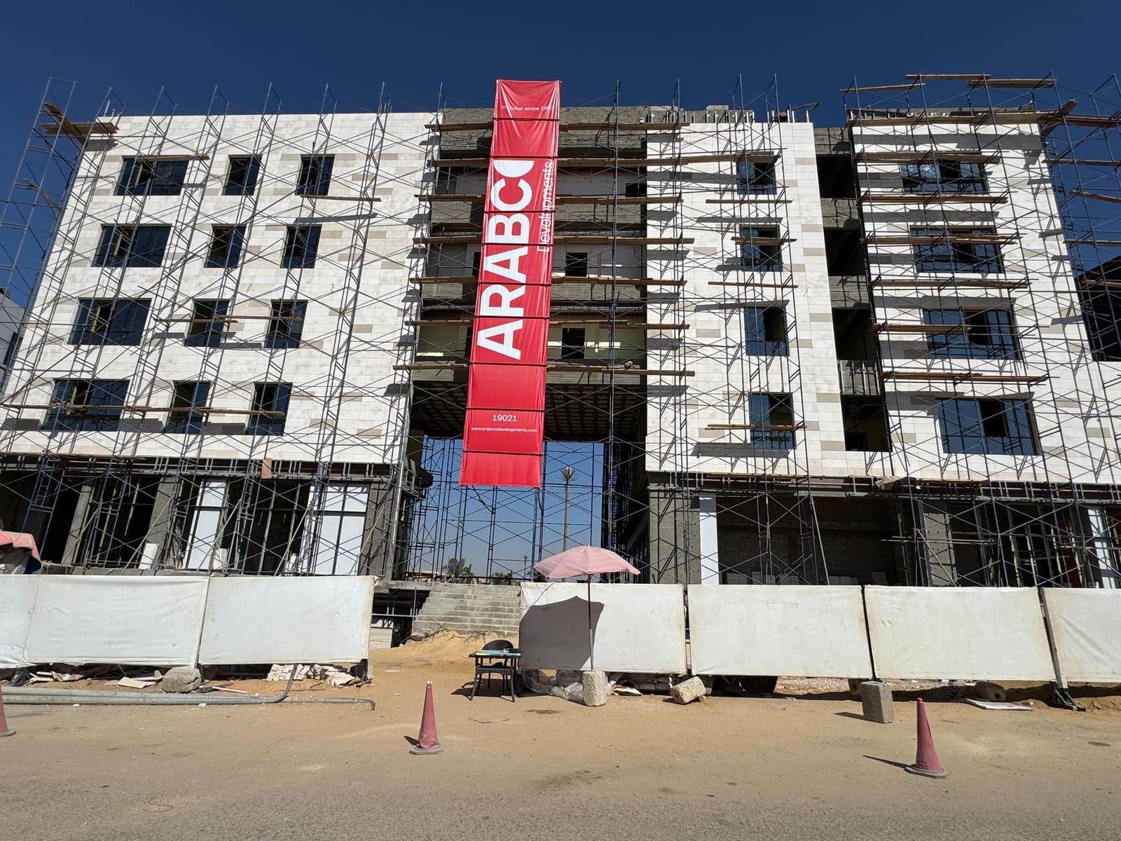 A multi-storey stone-clad commercial building under construction, wrapped in scaffolding beneath a clear sky